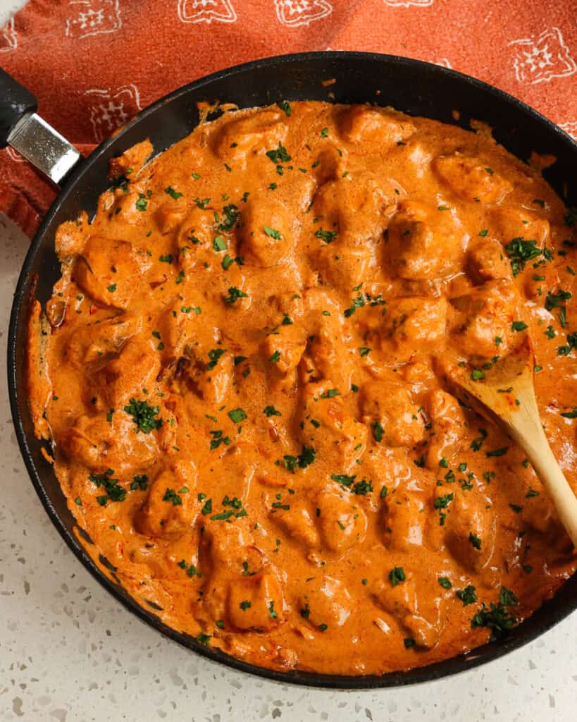 Chicken Paprikash in a large skillet before plating with a wooden spoon.