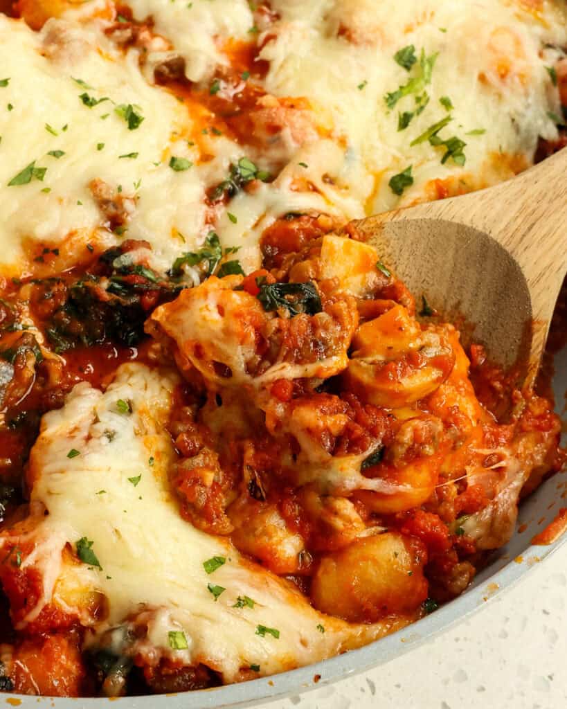 Baked Gnocchi on a wooden spoon topped with parsley.