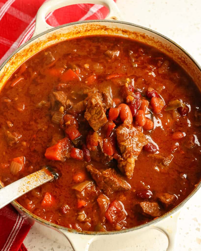 Chili con Carne in a big Dutch oven up close showing the dish on a laddle.