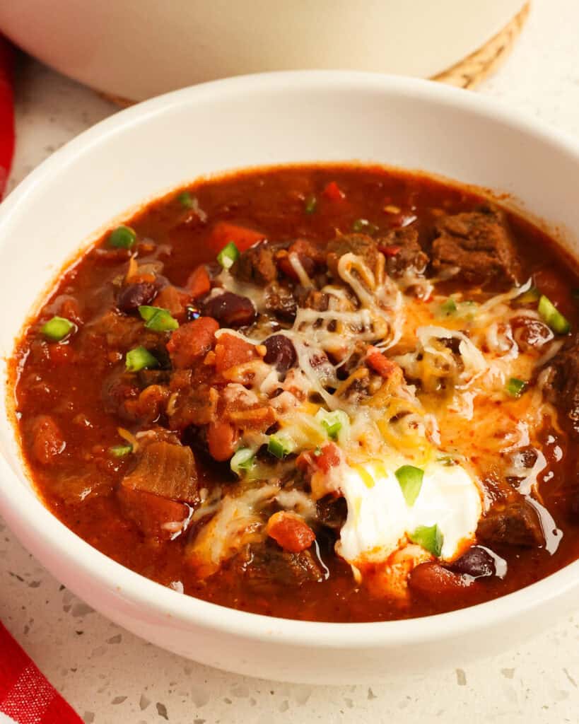 Chili con Carne in a white bowl topped with cheese, sour cream, and chopped jalapenos.