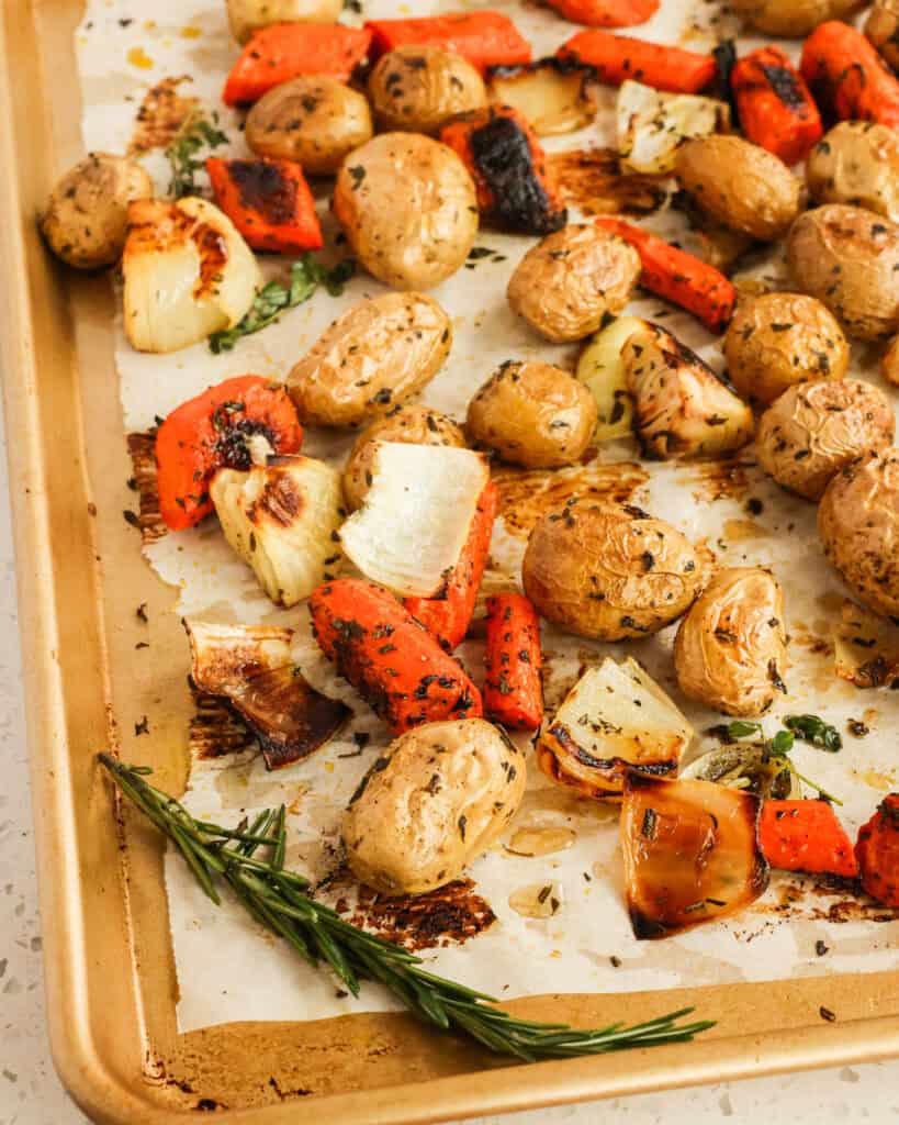 Roasted potatoes, carrots, and onions, on a baking sheet with parchment paper.