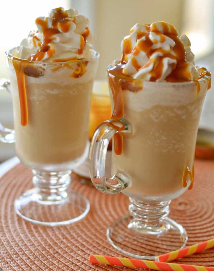 Two glass mugs full of caramel frappuccino topped with whipped cream and caramel sauce. 