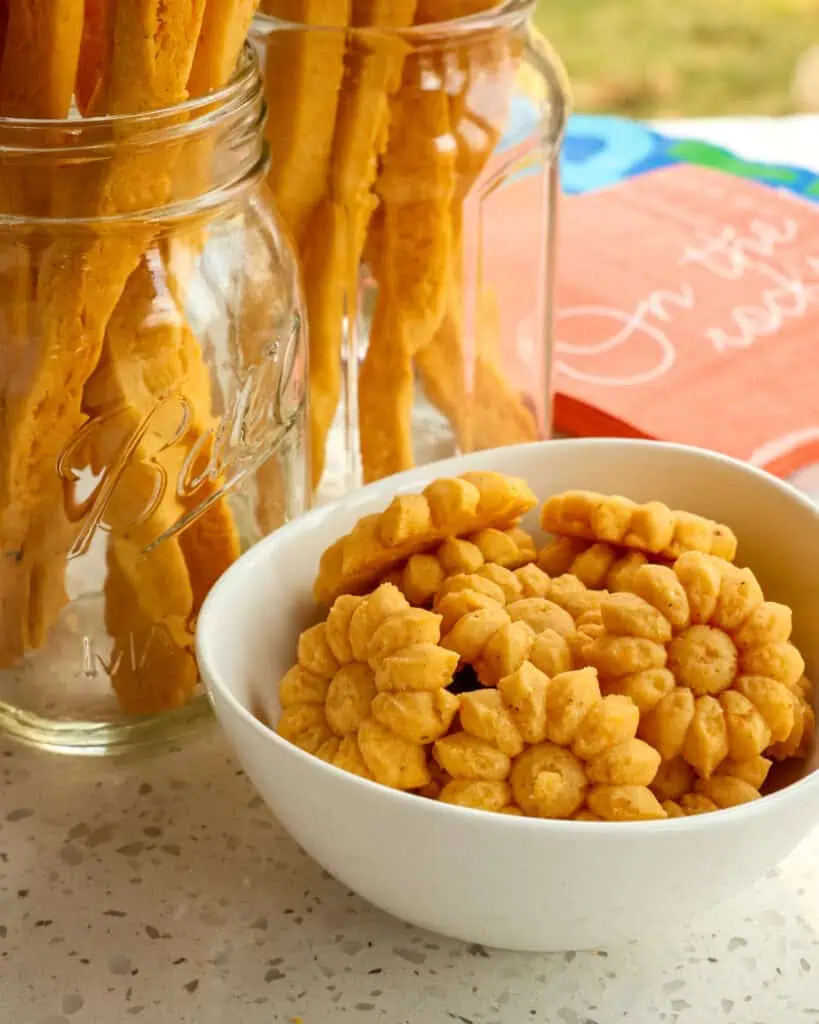 Cheese crackers in a bowl and cheese straws in large mason jars and cocktail napkins in the background. 
