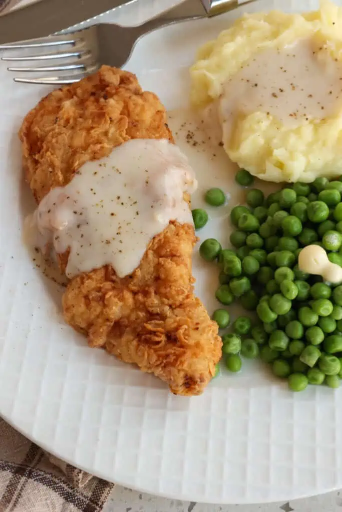 A quick and easy Southern Chicken Fried Chicken recipe with a crispy coating and creamy white country gravy. Enjoy it with mashed potatoes and sweet peas. 
