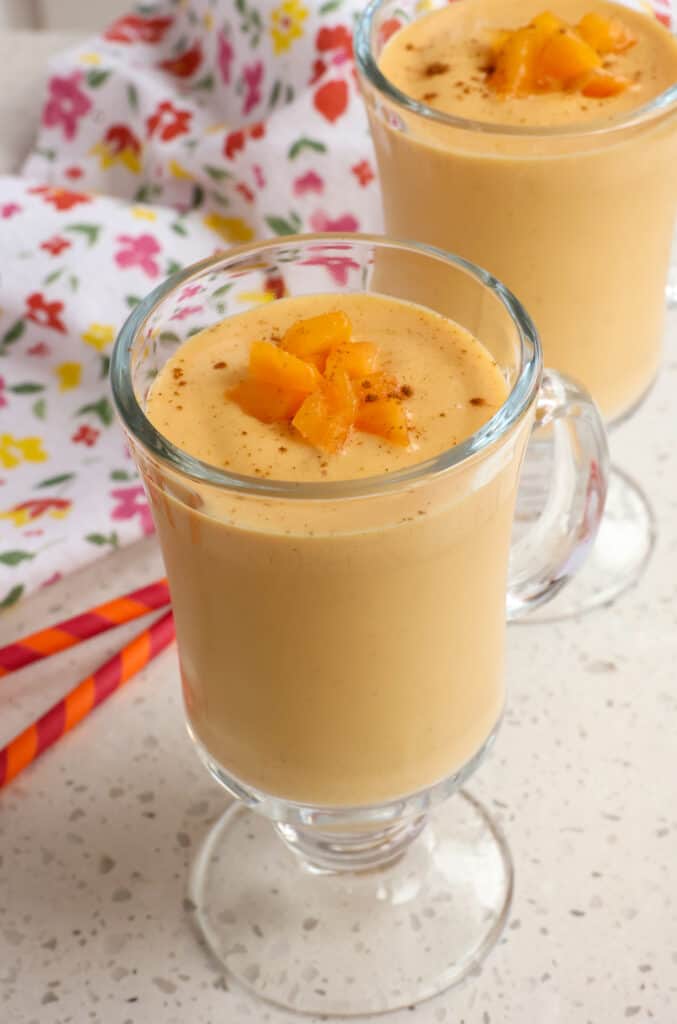 Two peach smoothies in glasses garnished with chopped peaches and cinnamon. 