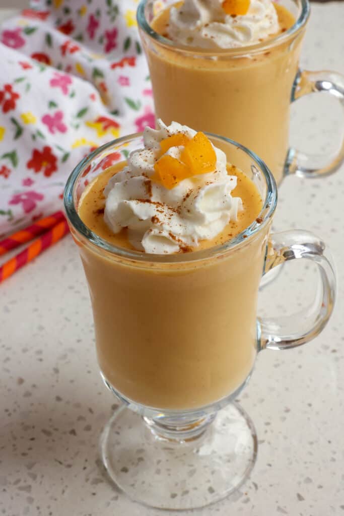 Peach smoothie is a glass garnished with whipped cream, chopped peaches and a sprinkle of cinnamon. 