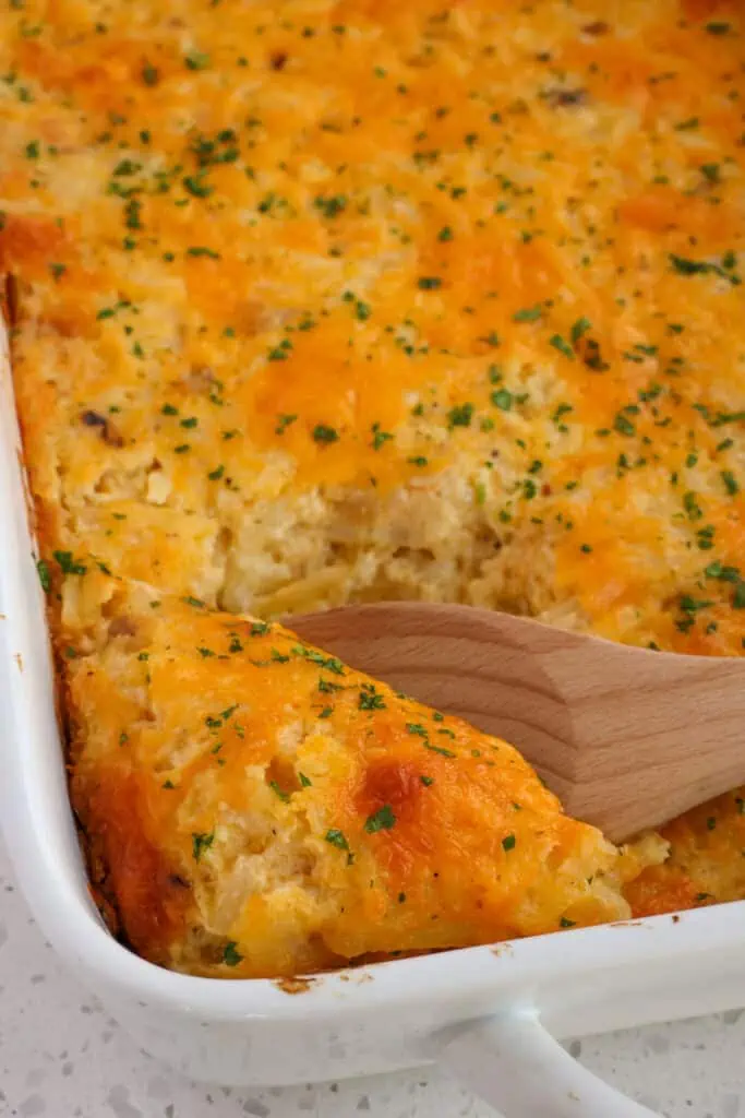 This foolproof hashbrown casserole recipe starts with thawed frozen shredded hash brown potatoes combined with sauteed onions and garlic, sour cream, butter, and a generous portion of cheddar cheese.