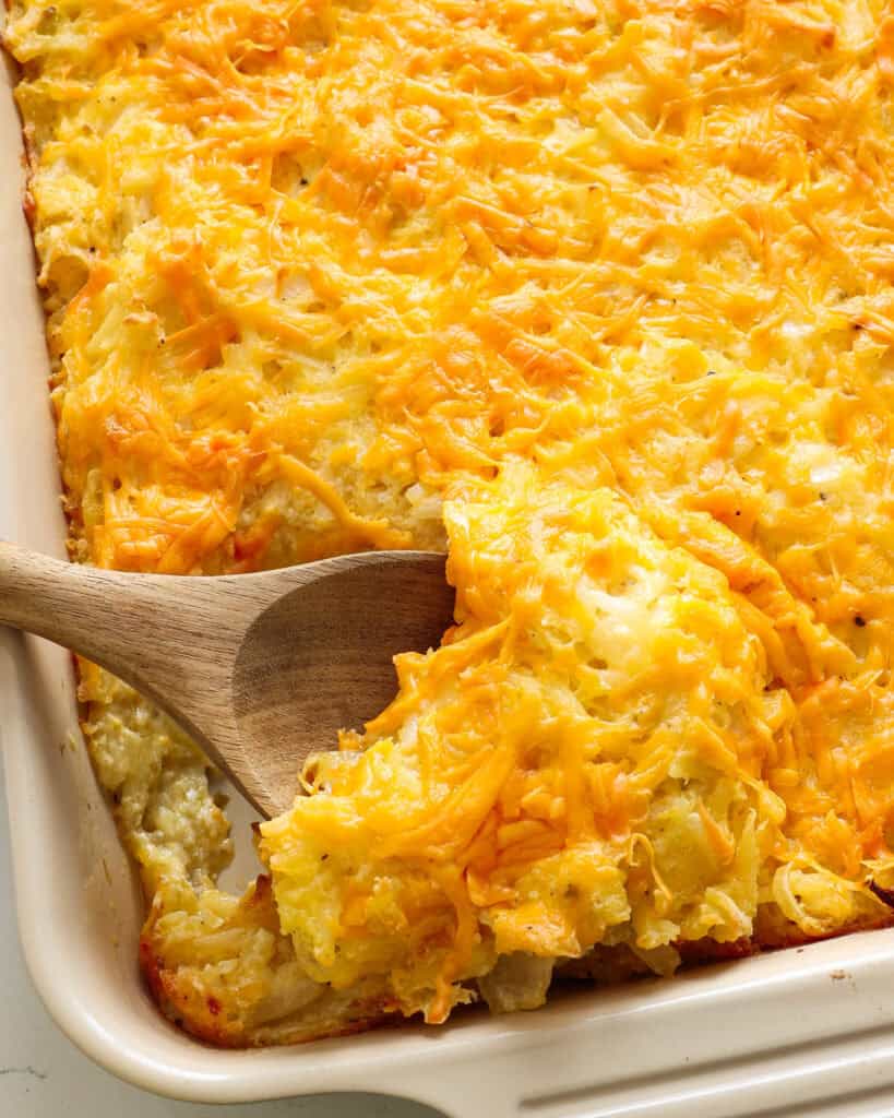 A casserole and wooden spoon full of cheesy hashbrown casserole. 