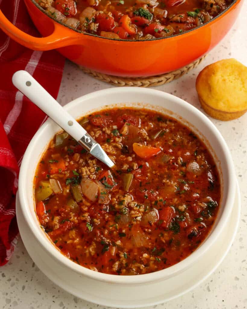 An individual soup bowl full of stuffed pepper soup with a corn muffin in the background.