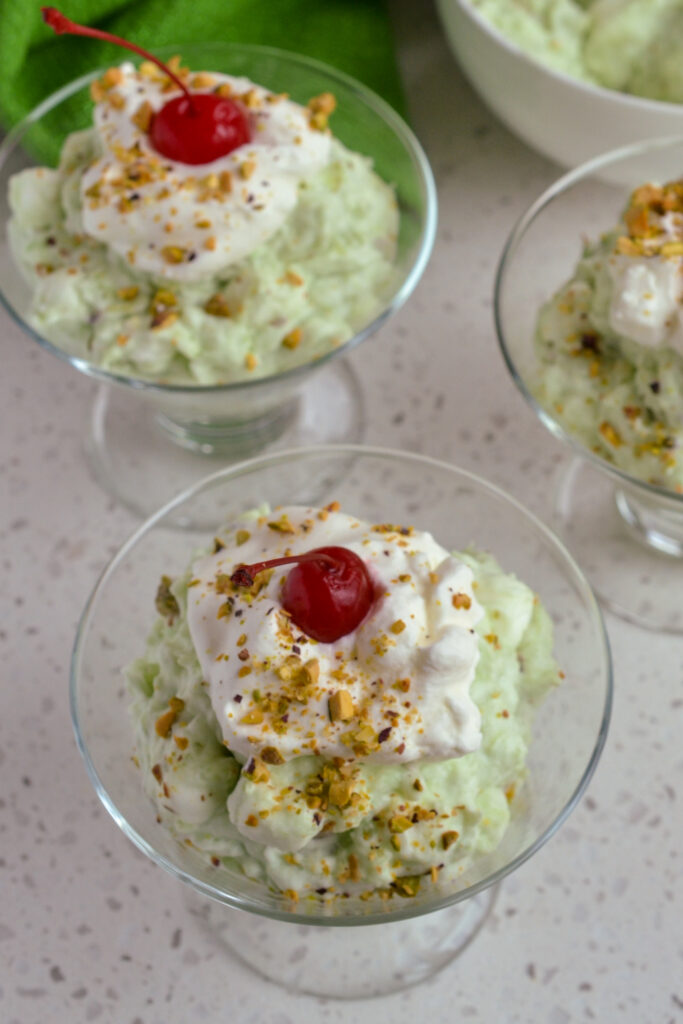 Individual dessert cups filled with watergate salad, whipped cream, nuts and a cherry. 