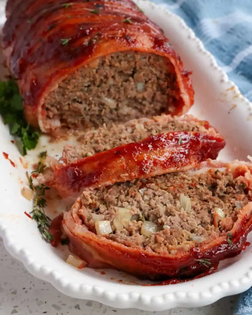 Sliced bacon wrapped meatloaf on a white serving platter. 