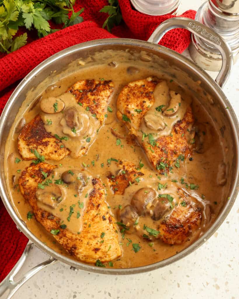 An overheadview of Cajun chicken and sauce in a large skillet with salt and pepper shaker and italian parsley in the background. 