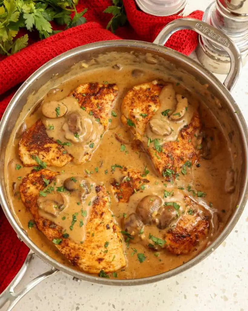 An overheadview of Cajun chicken and sauce in a large skillet with salt and pepper shaker and italian parsley in the background. 