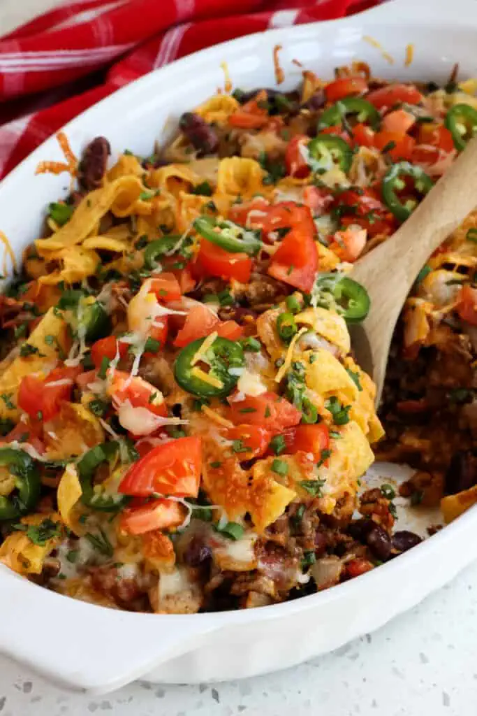 A Frito Pie recipe loaded with seasoned ground beef, sweet onions, tomatoes, beans, and Fritos all topped with a generous helping of Cheddar Cheese and Monterey Jack Cheese and baked to golden perfection. 