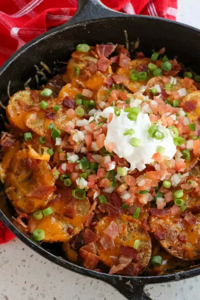 Crispy roasted seasoned potato rounds are loaded with cheddar cheese, crispy bacon, green onions, tomatoes, and sour cream.