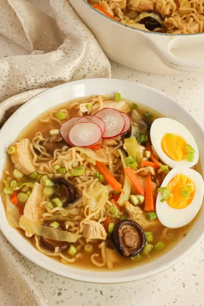 Easy Chicken Ramen combines pan-seared chicken breasts, shiitake mushrooms, carrots, cabbage, and ramen noodles in rich chicken stock, all garnished with sliced radishes, onions, and a soft-boiled egg.