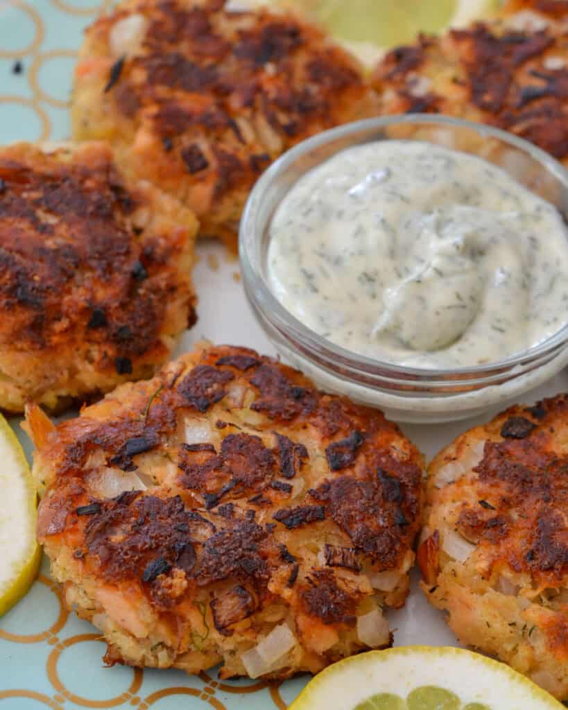 Salmon Patty Recipe Six salmon pattties on a plate with lemons and dill mayonnaise.