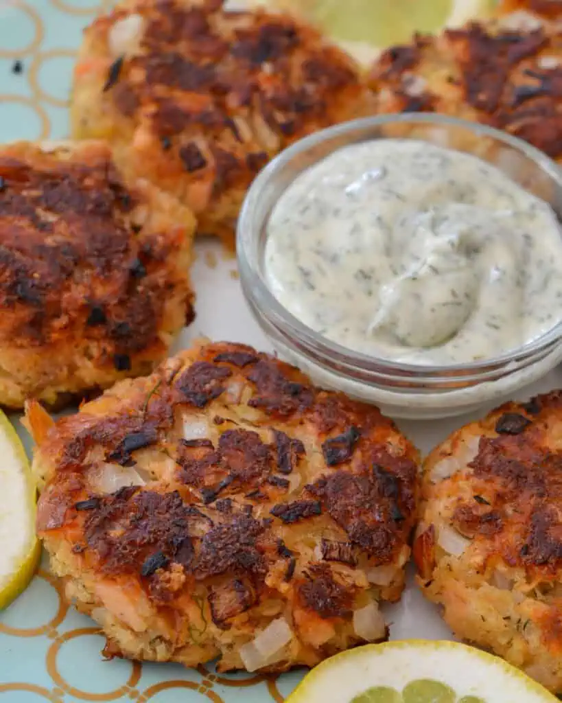 Six salmon pattties on a plate with lemons and dill mayonnaise. 
