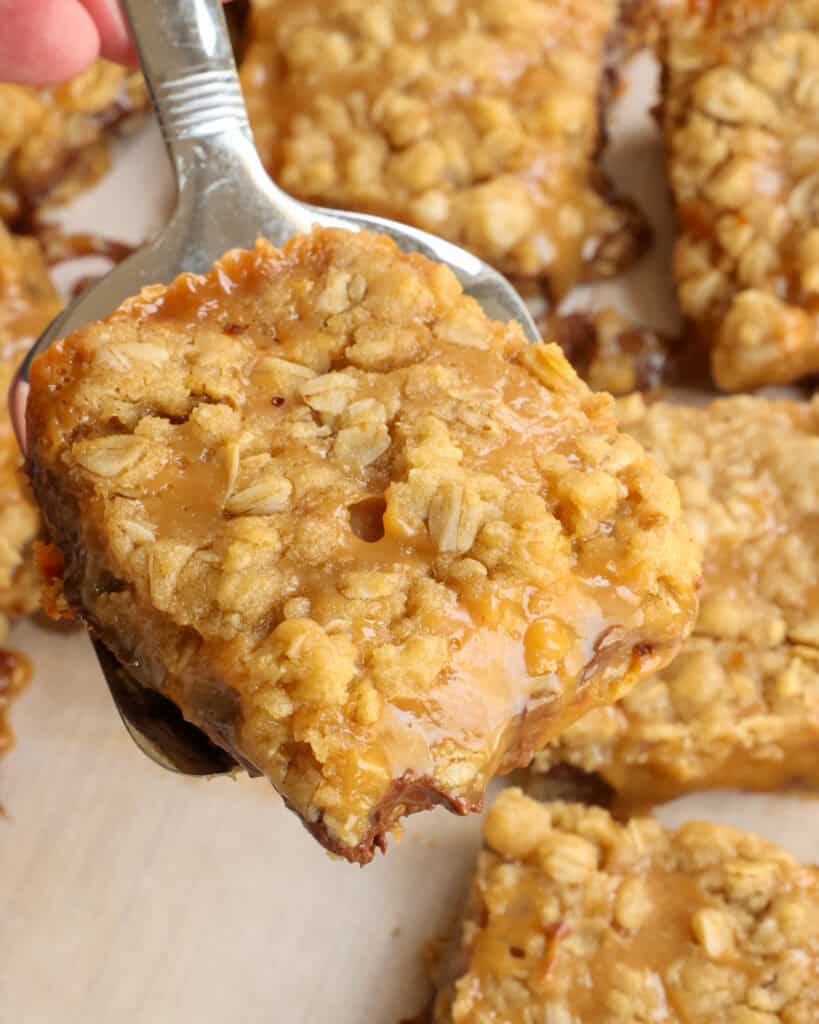 A close up view of a carmelita bar on a spatula with caramel oozing out. 