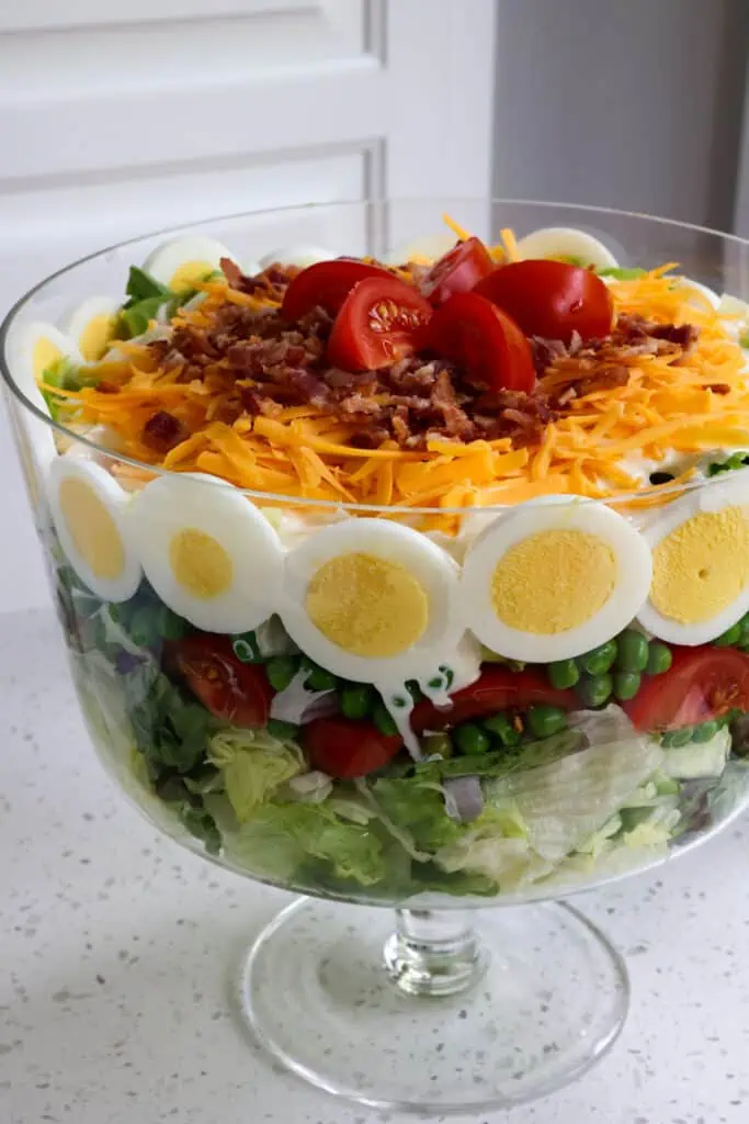 A delectable layer salad with peas, eggs, bacon, cheddar, and a four-ingredient creamy mayonnaise dressing.  It is perfect for a potluck, game day, family gatherings, and neighborhood socials.