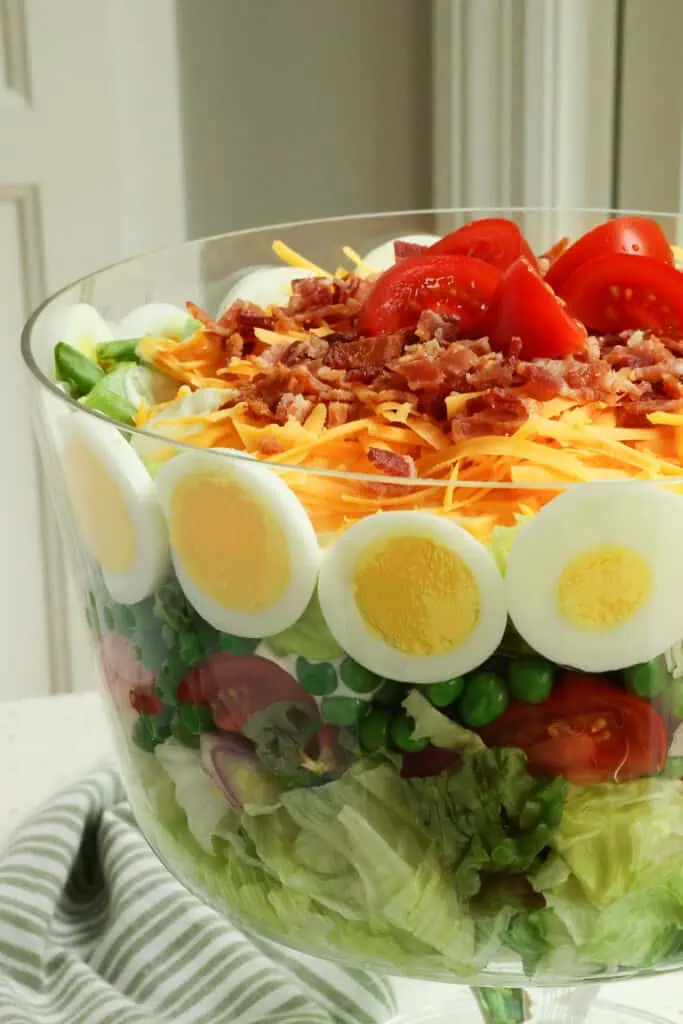 This classic Seven Layer Salad is a real crowd-pleaser with sun-ripened tomatoes, sweet peas, hard-boiled eggs, crisp bacon, and sharp cheddar cheese.
