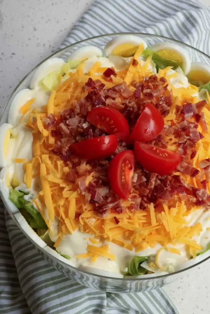 A delectable layer salad with peas, eggs, bacon, cheddar, and a four-ingredient creamy mayonnaise dressing.  It is perfect for a potluck, game day, family gatherings, and neighborhood socials.