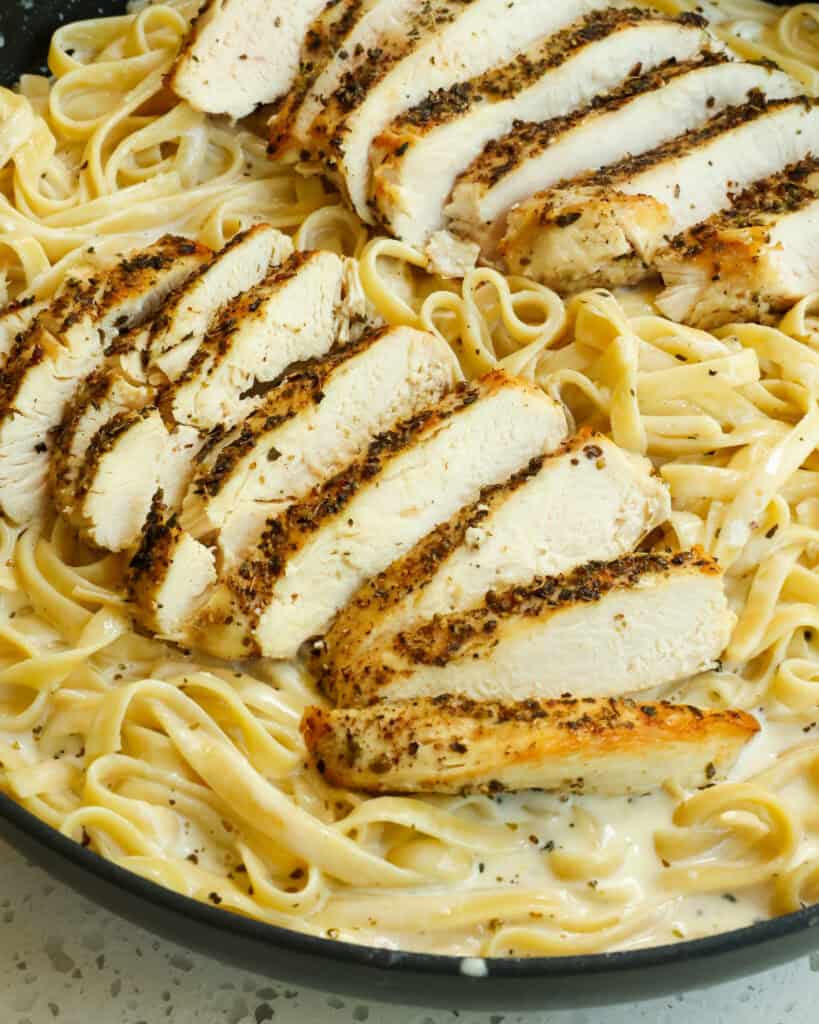 Fettuccine alfredo with sliced seasoned chicken on top.