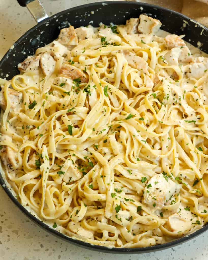 A large skillet full of chicken fettuccine alfredo with chopped fresh Italian parsley.