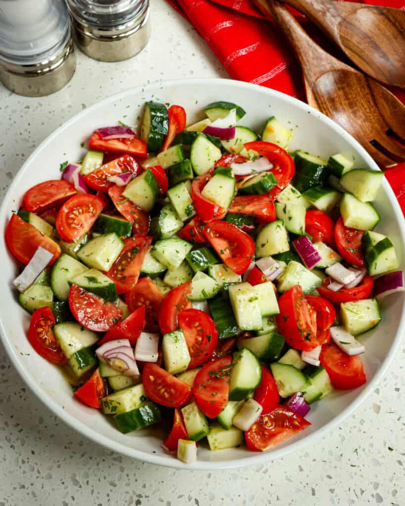 An overhead view of cucumber tomato salad in a large white serving bowl. 