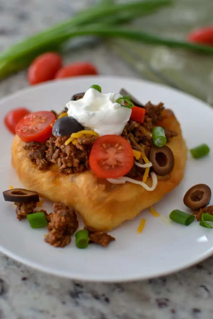 Spoon the taco meat onto the warm bread. Top with shredded cheese, tomatoes, green onions, black olives, and sour cream. 