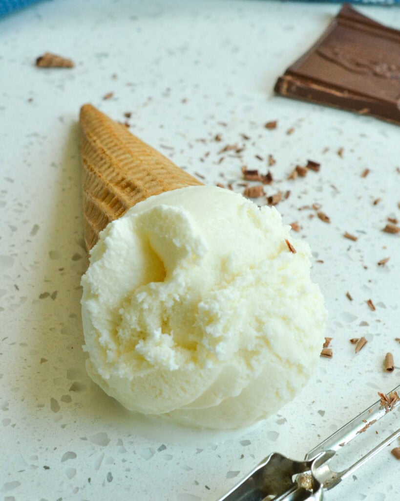 Vanilla Ice Cream in a cone laid down with chocolate shavings spread around.