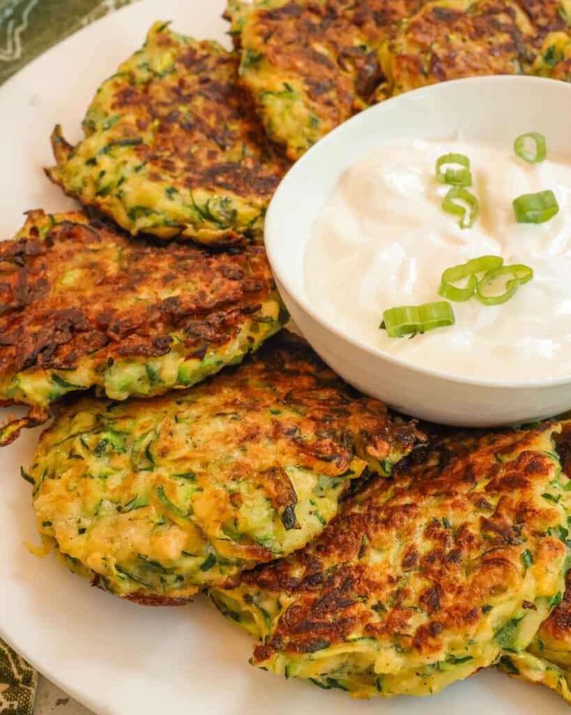 Zucchini Fritters on a white plate with a dipping sauce.
