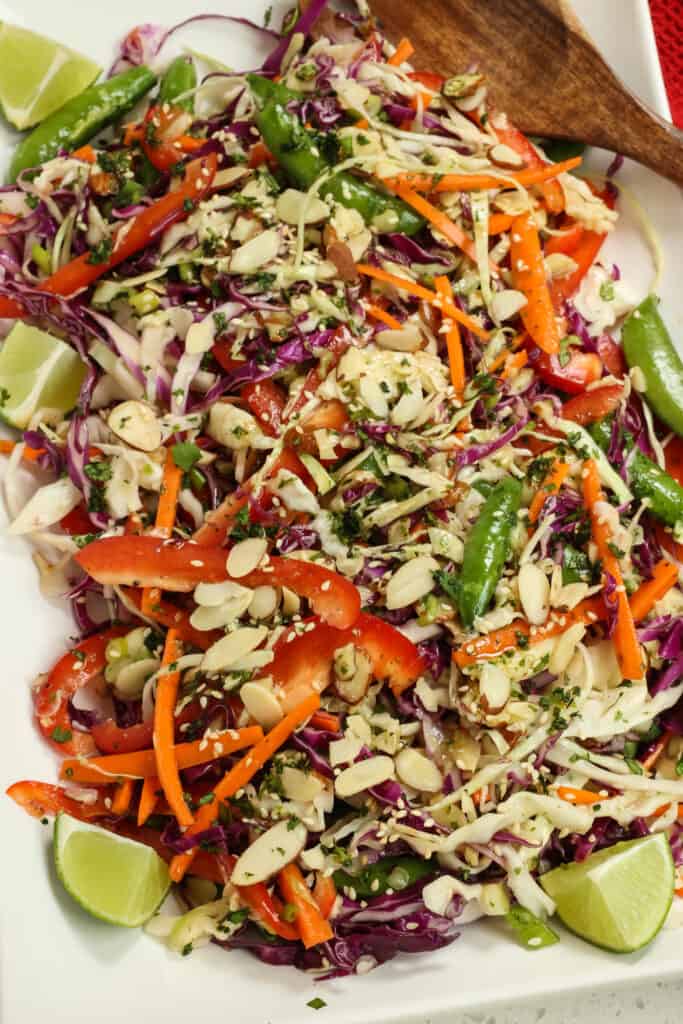 Add the red and green cabbage, bell pepper, carrots, sugar snap peas, sliced almonds, green onions, sesame seeds, and chopped cilantro to a large bowl. 
