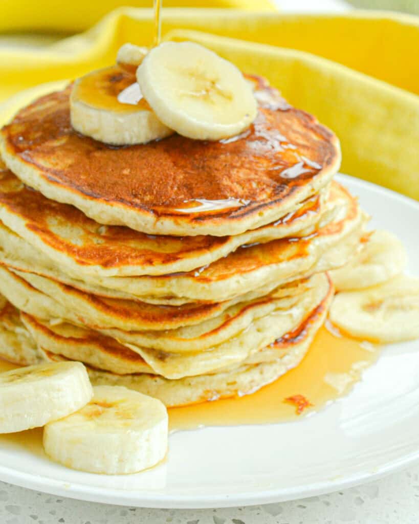 A stack of banana pancakes with syrup and slices of banana on a single serving plate.