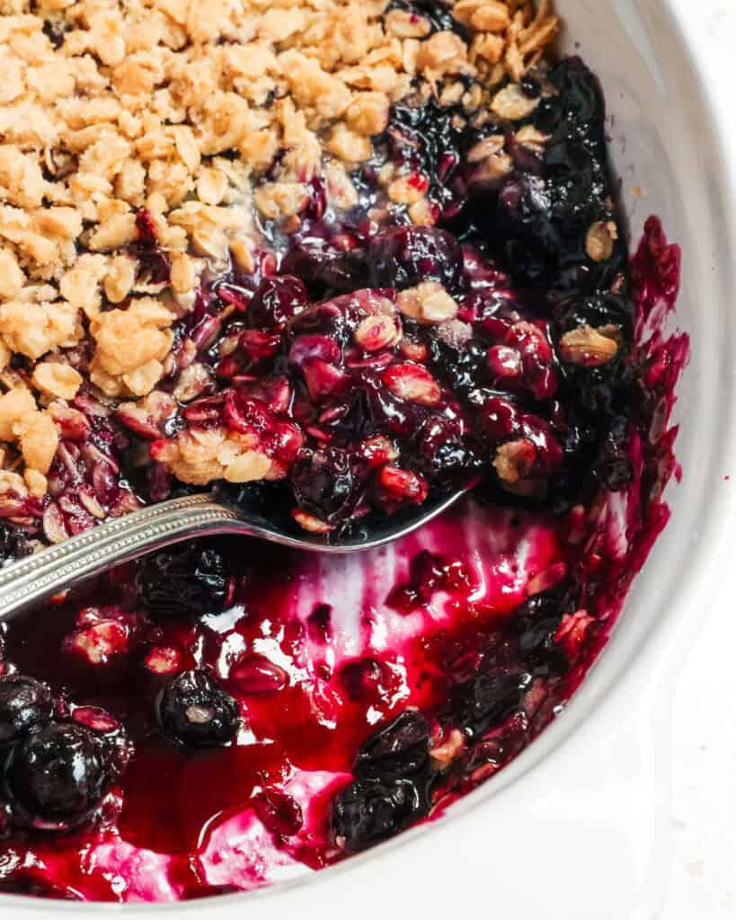 A close up view of blueberry crisp with a spoon full of blueberry crisp in it. 