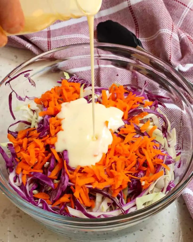 A bowl full of tri color coleslaw mix with creamy coleslaw dressing  being poured in it. 