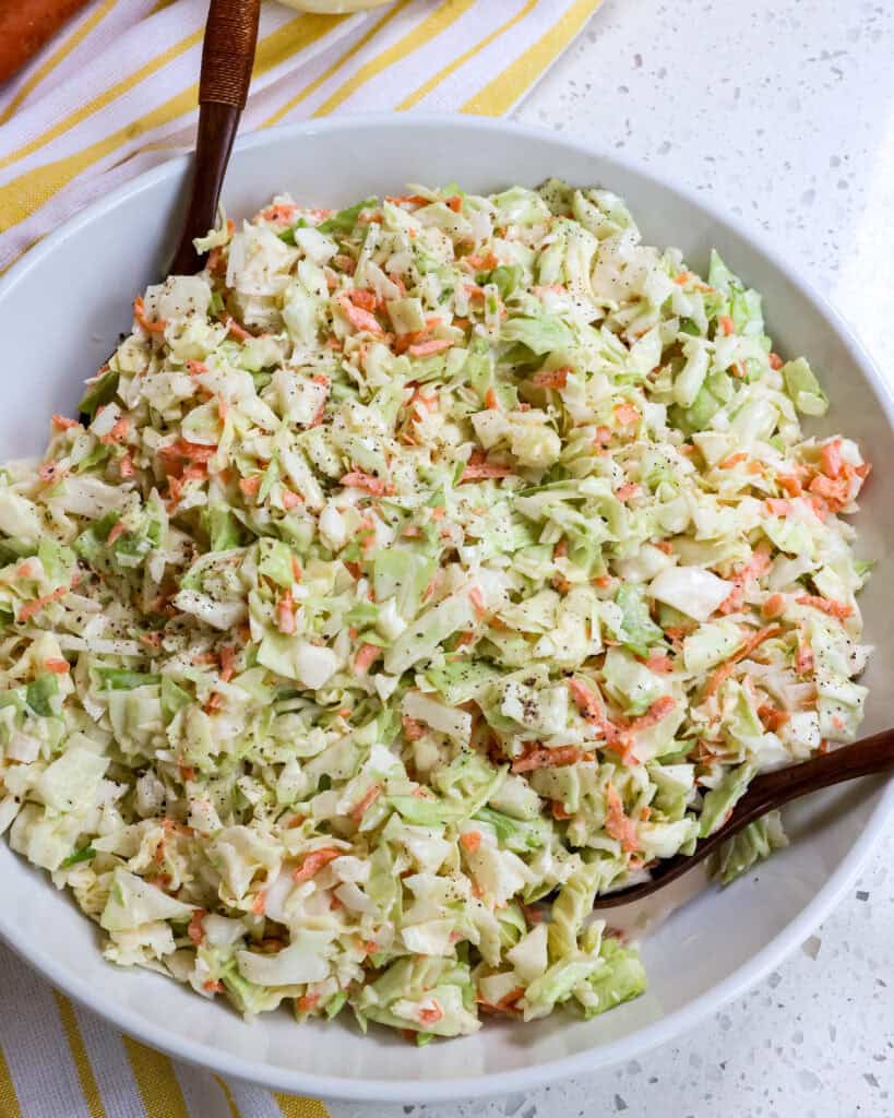 Creamy Coleslaw in a large white bowl with two wooden spoons.