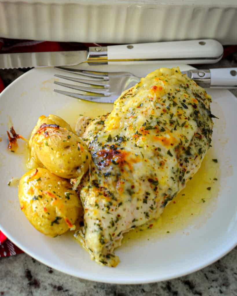 Garlic butter chicken and potatoes on a white serving plate with a fork and a knife. 