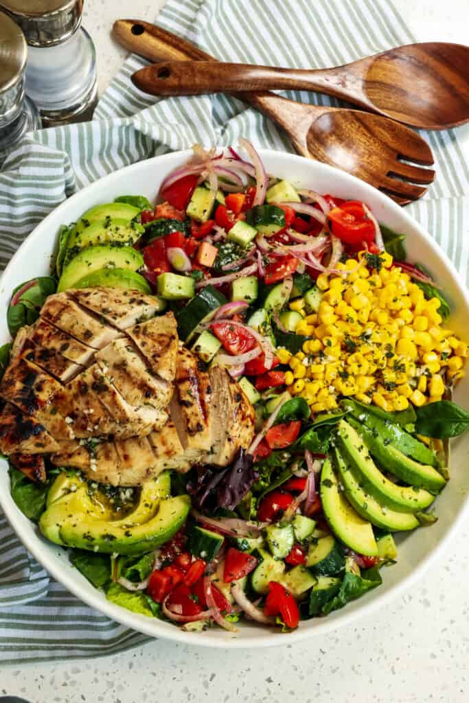 Arrange the mixture and the corn kernels over the greens. Cut the chicken breast and arrange it over the salad greens. Pit the avocados, peel, and slice. Arrange them over the greens and brush them with lemon or lime juice. Drizzle with the remaining dressing and serve. 
