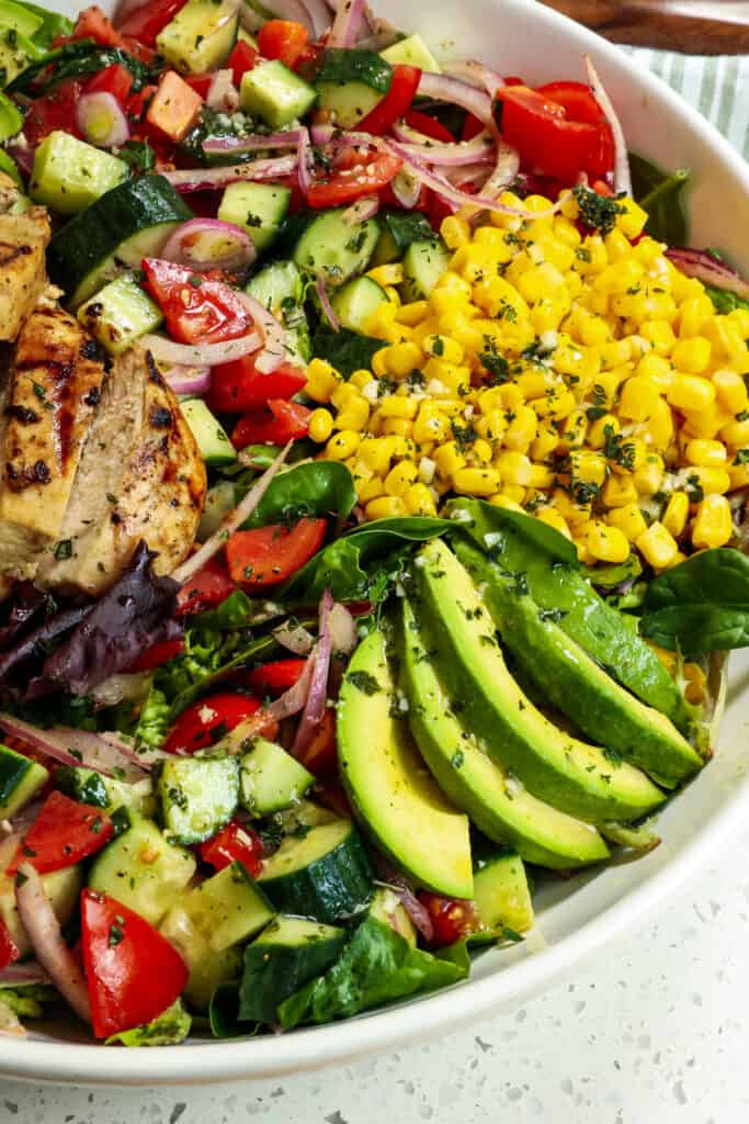A delicious Grilled Chicken salad with tomatoes, cucumbers, red onions, corn, and avocado, all drizzled with tangy mustard ginger vinaigrette. Summer never tasted so good! 