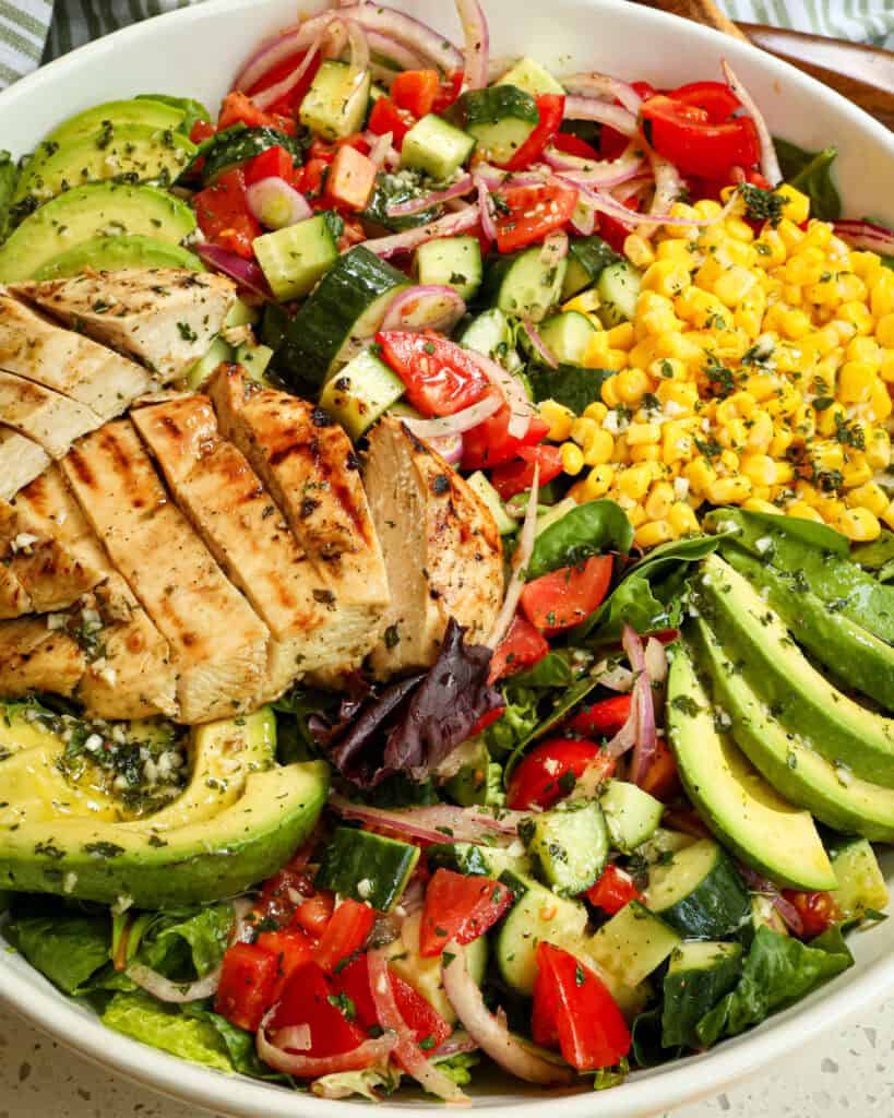 A close up view of grilled chicken salad in a large white serving bowl. 