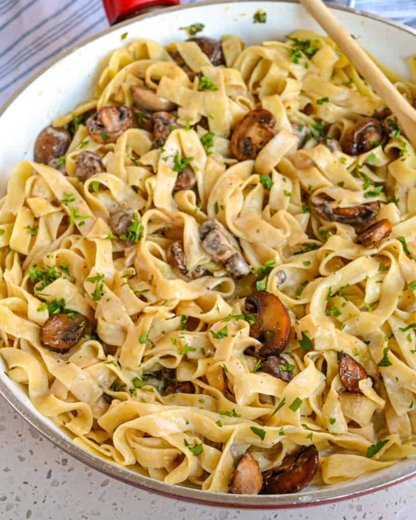 A skillet and a wooden spoon full of mushroom pasta. 