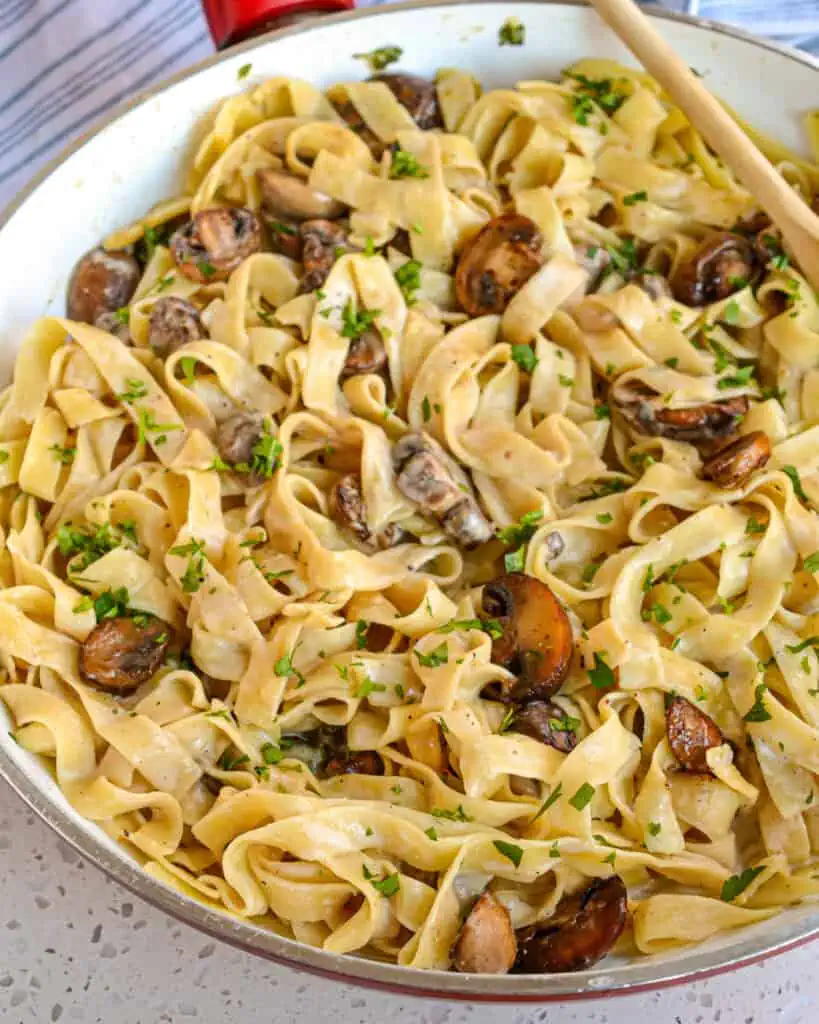 A skillet and a wooden spoon full of mushroom pasta.