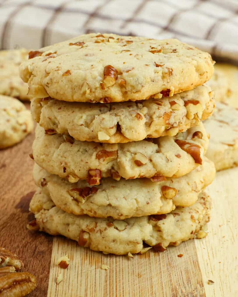 A stack of pecan sandies on a wooden cutting board with more cookies in the background. 