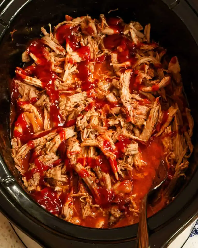 An overhead view of barbecued pulled pork in a black slow cooker.