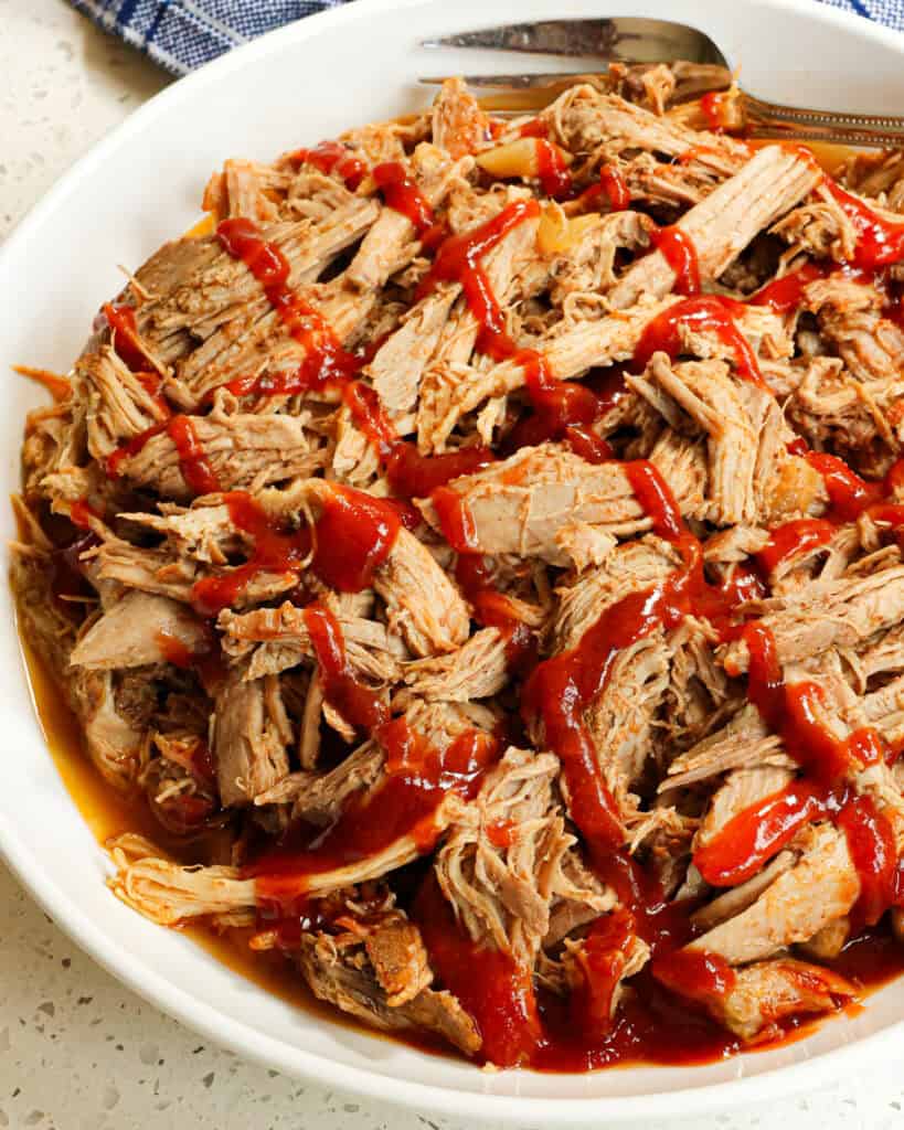 A white serving bowl full of crockpot pulled pork drizzled with barbecue sauce. 