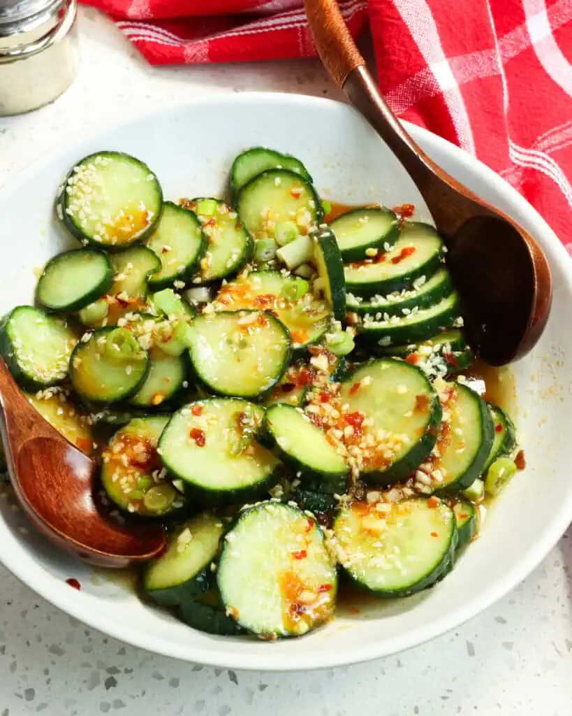A serving bowl full of Asian cucumber salad with two wooden serving spoons in it. 