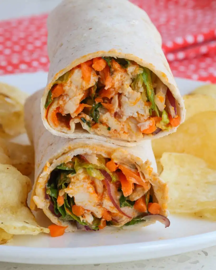 A halved buffalo chicken wrap with carrots, romaine, red onion, and cheese. 
