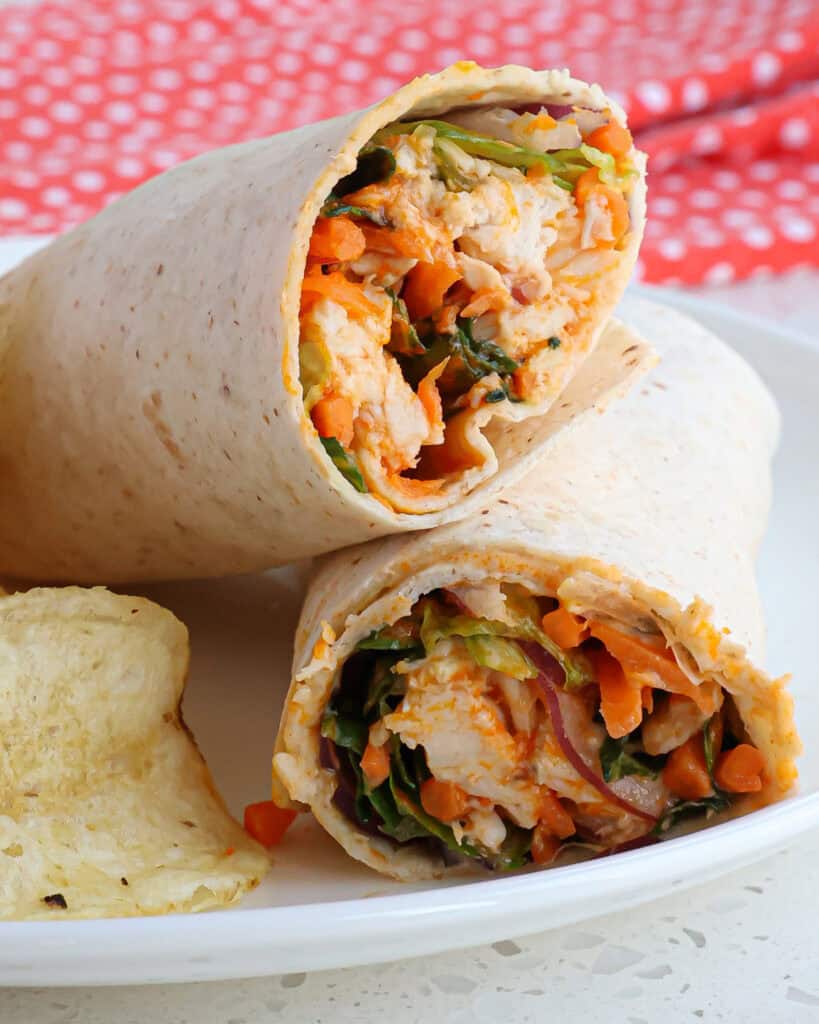 A halved buffalo chicken wrap with carrots, romaine, red onion, and cheese. 