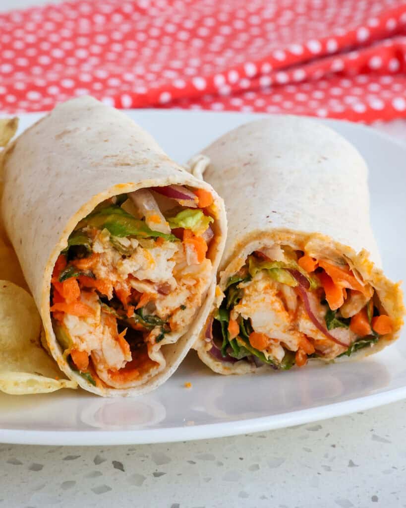 A halved buffalo chicken wrap on a plate with potato chips. 